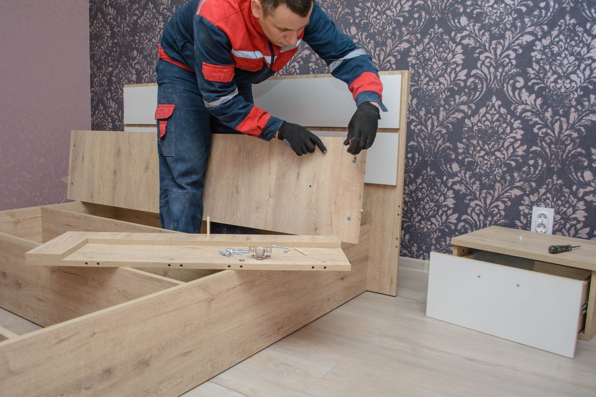 Assembling new wooden bed by hand in room. Man putting together new furniture.