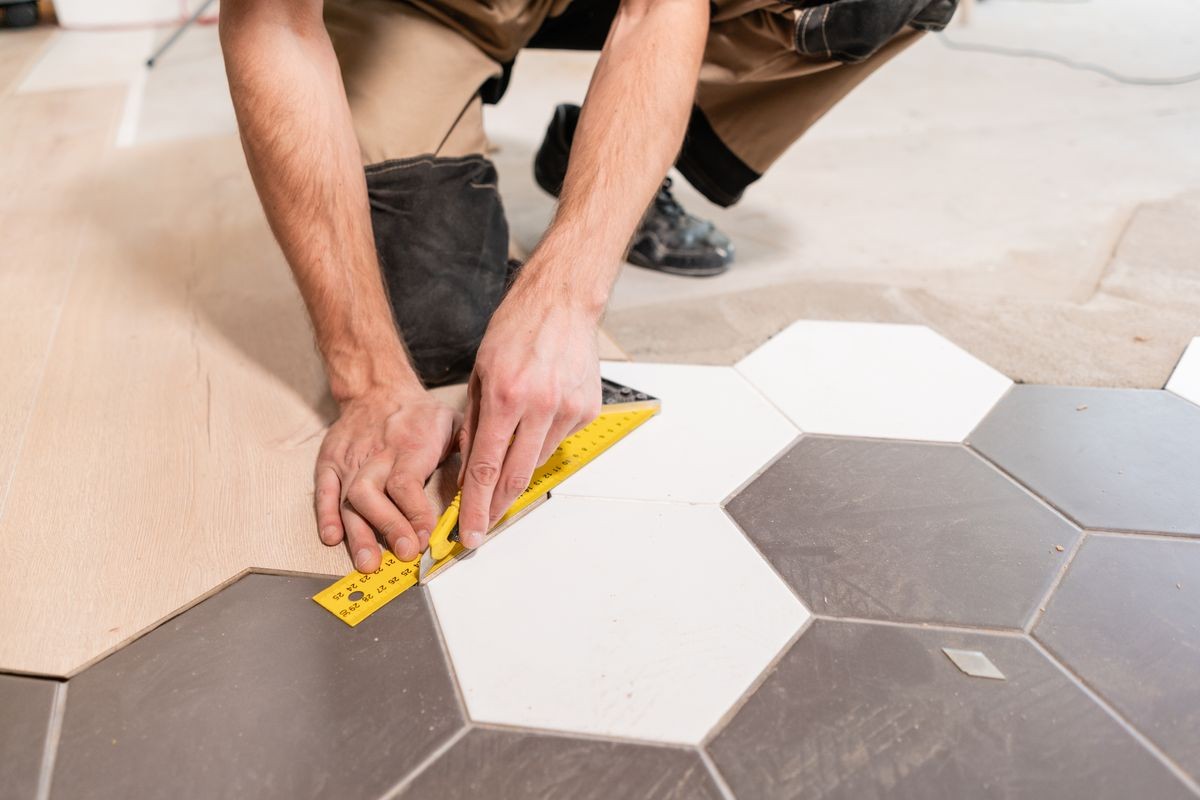 Male worker makes measurements and installing new wooden laminate flooring. The combination of wood panels of laminate and ceramic tiles in the form of honeycomb. Kitchen renovation.